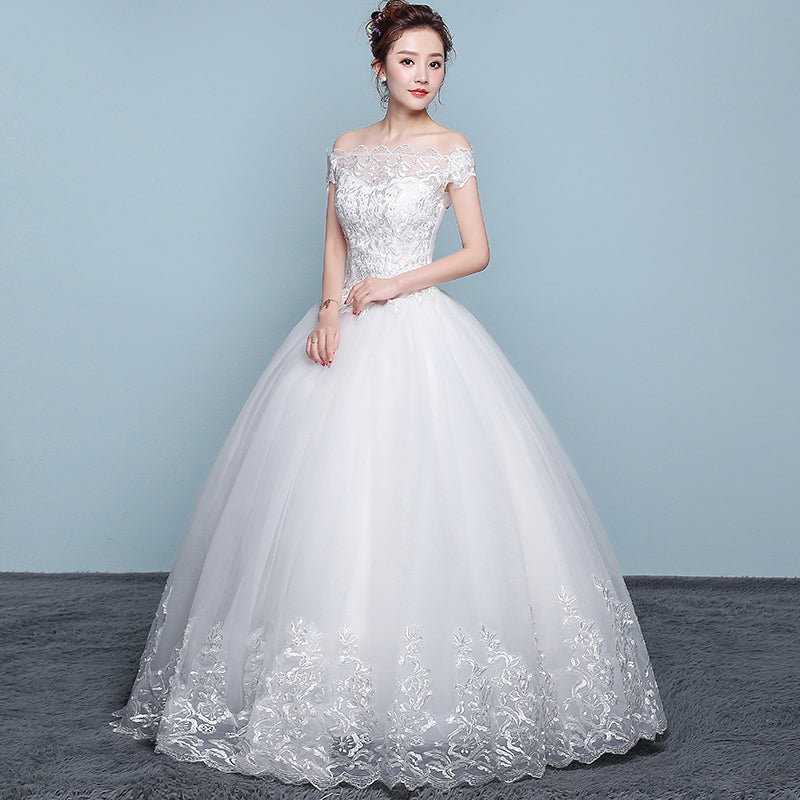 Woman wearing a white wedding dress with floral lace details on a gray background