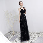 Woman in a black evening gown with floral embroidery standing on a white surface.
