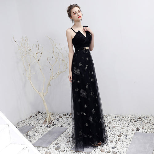 Woman in a black evening gown with floral embroidery standing on a white surface.