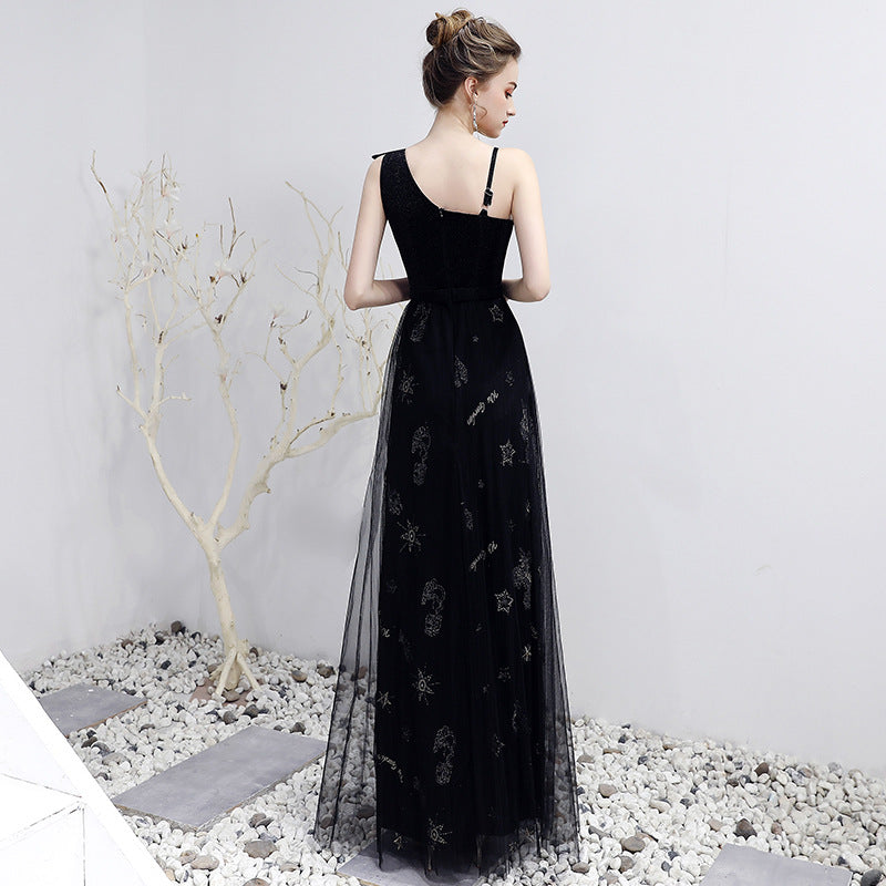 Woman wearing a black evening gown with floral embroidery in an indoor setting.