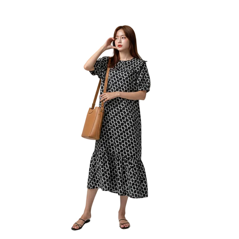 Woman in a black and white polka dot dress holding a yellow bag outdoors.
