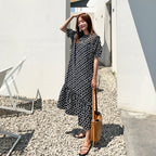 Woman in a black and white polka dot dress standing outdoors near a white building.