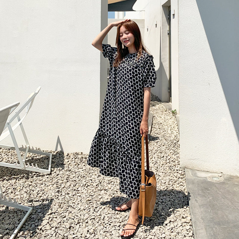 Woman in a black and white polka dot dress standing outdoors near a white building.