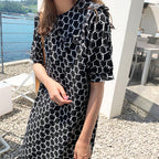 Person wearing a black and white patterned dress by a waterfront.