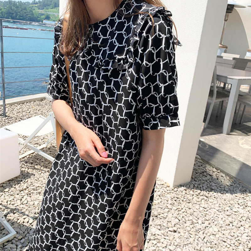 Person wearing a black and white patterned dress by a waterfront.