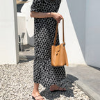 Woman holding a brown leather handbag wearing a black and white patterned dress.