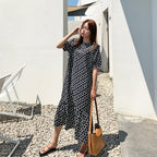 Woman in a black and white polka dot dress holding a yellow bag outdoors.
