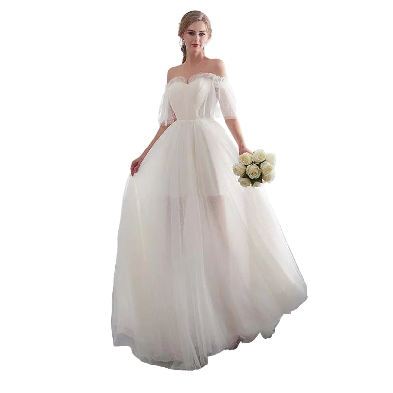 Woman in a white wedding dress holding flowers in a bright room with white curtains.