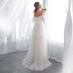 Woman in a white wedding dress holding flowers in a bright room with sheer curtains.