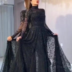 Woman wearing a black sequin dress with sheer sleeves in an indoor setting.