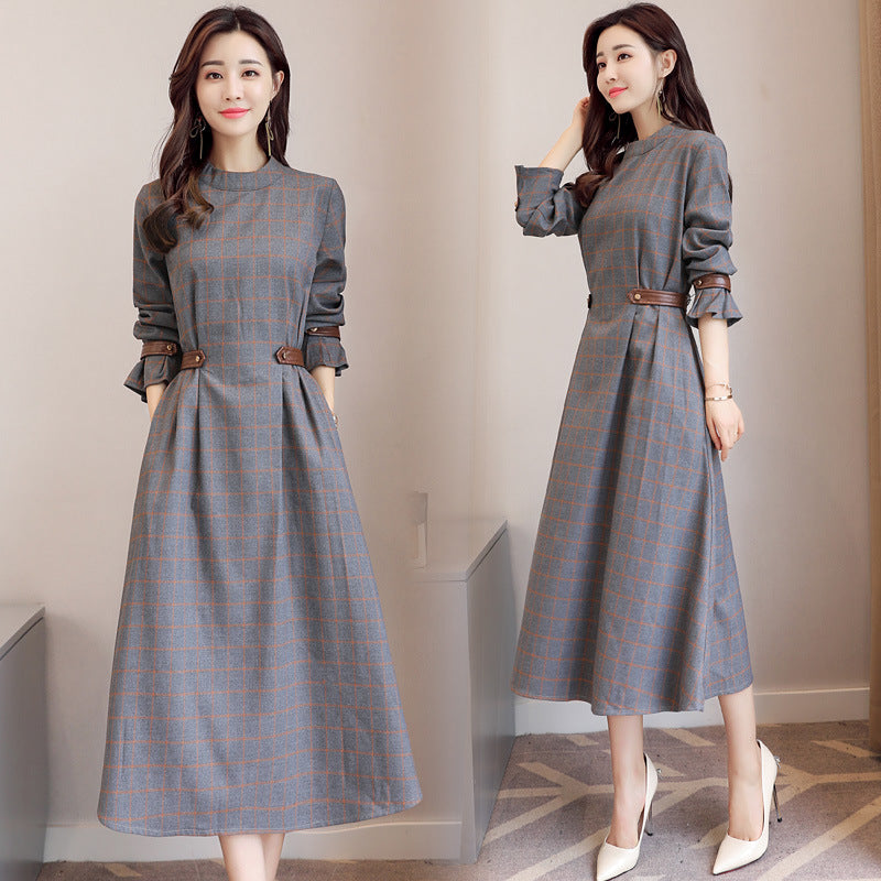 Woman wearing a gray plaid dress with brown belt in a room.