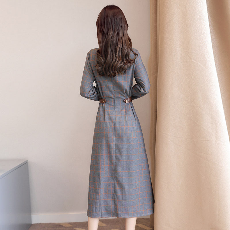 Woman wearing a gray plaid dress standing in a room with beige curtains.