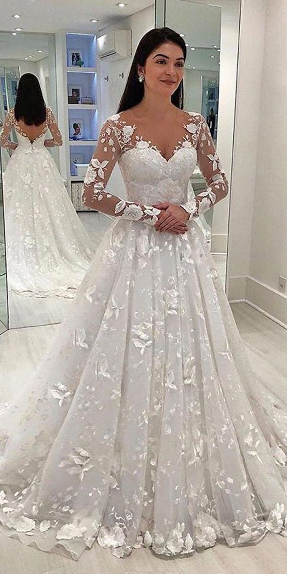 Woman wearing a white wedding dress with floral details in a mirror reflection.