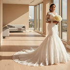 Bride in a white lace wedding dress holding flowers in front of a house.