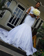 Bride in a white lace wedding dress holding flowers in front of a house.