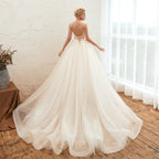 Woman in a white wedding dress standing in a room with wooden floor and white curtains.