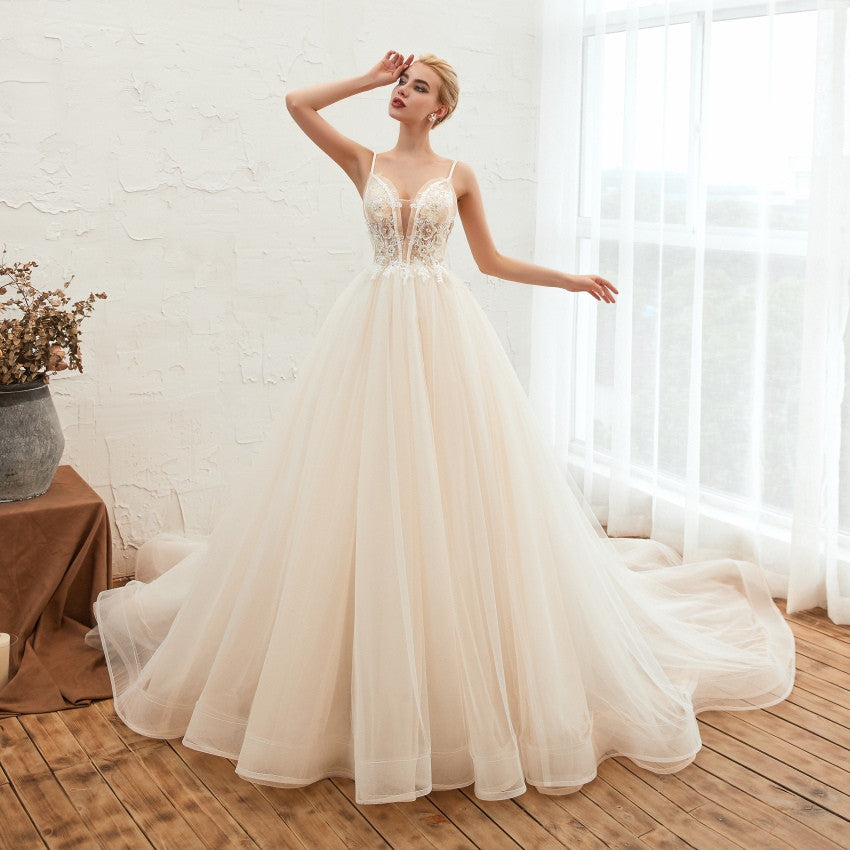Woman in a flowing white wedding dress standing in a bright room with large windows.