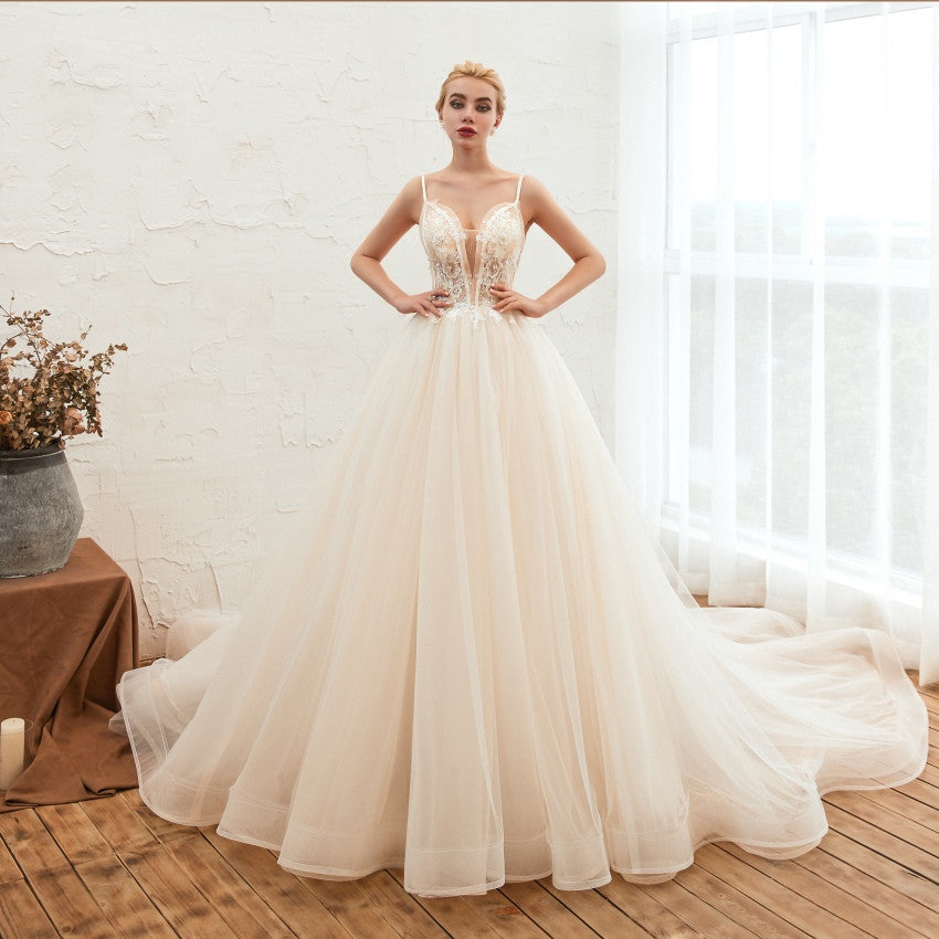 Woman in a white wedding dress standing in a bright room with a vase of flowers on a table.