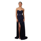 Woman wearing a strapless, sequined evening gown with a high slit on a gray background.