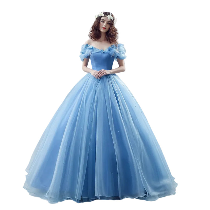 Woman in a blue ball gown standing in a decorated room with flowers and mirrors.