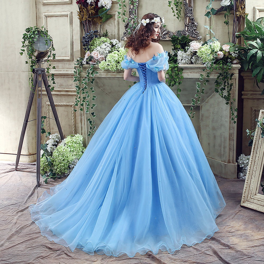 Woman in a blue evening gown standing in a decorated room with flowers and mirrors.