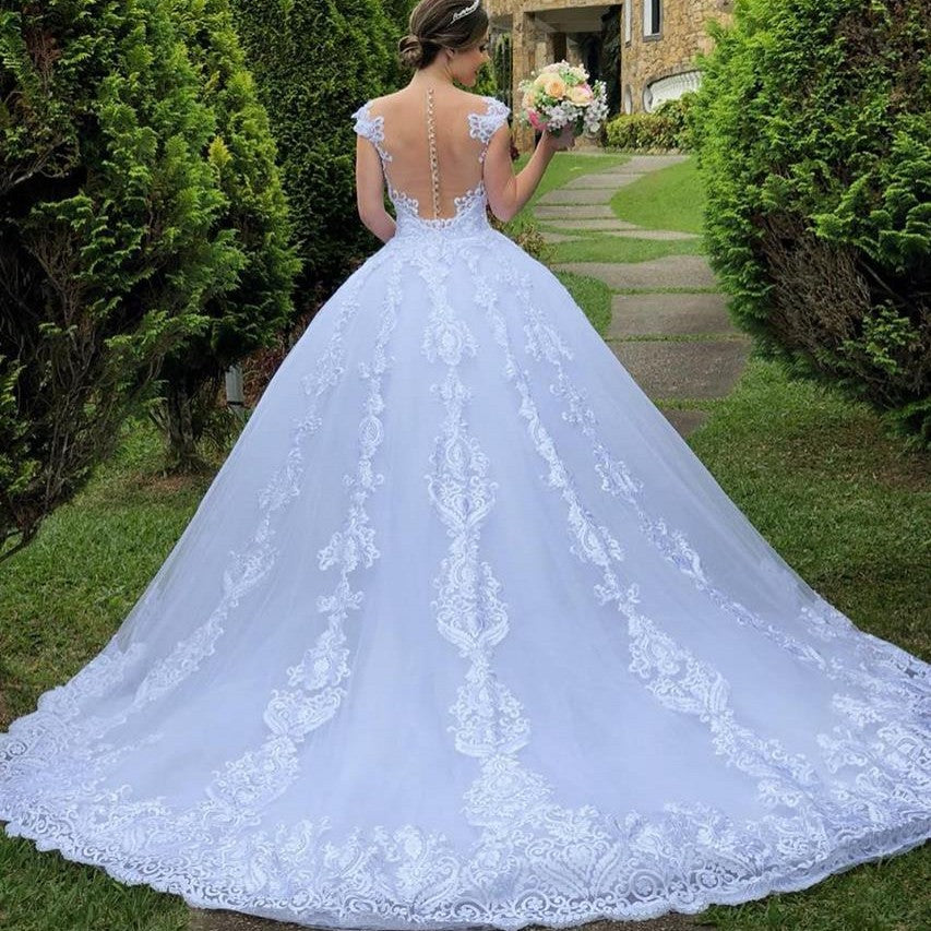 Woman in a white lace wedding dress holding a bouquet in an outdoor setting.