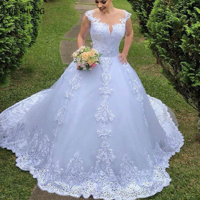 Woman in a white lace wedding dress holding a bouquet outdoors.