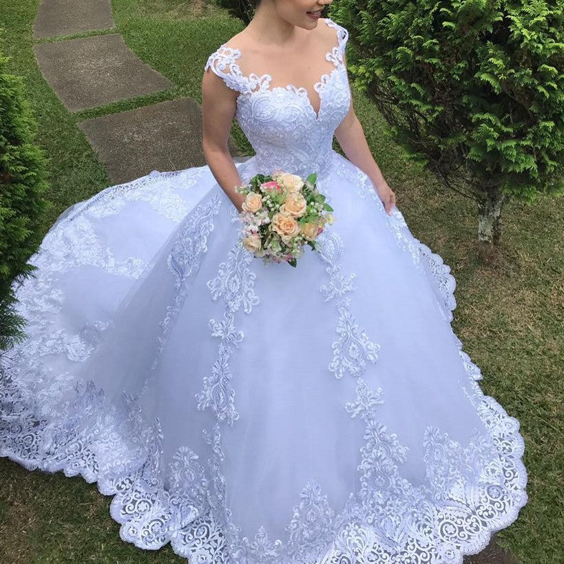 Woman in a white lace wedding dress holding a bouquet outdoors.