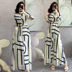 Woman wearing a long white dress with blue geometric patterns, standing in front of a marble wall.
