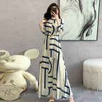 Woman in a long dress with geometric pattern standing in a room with a large teddy bear and abstract art on the wall.