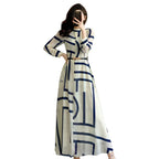 Woman in a long white dress with blue geometric patterns taking a mirror selfie in a modern room.