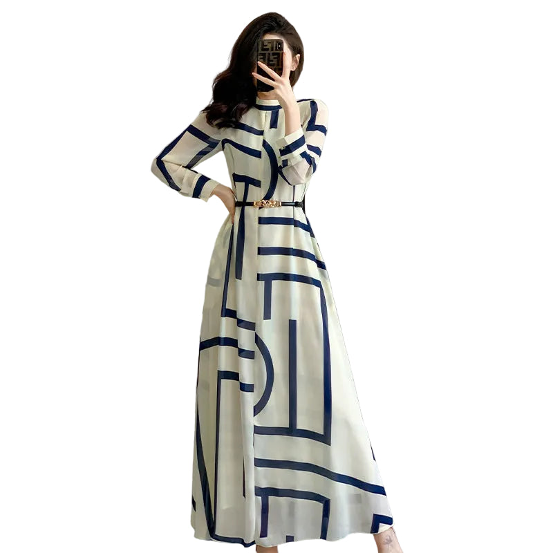 Woman in a long white dress with blue geometric patterns taking a mirror selfie in a modern room.