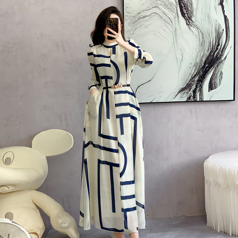 Person wearing a white dress with blue geometric patterns, standing in a room with abstract art on the wall.