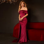 Woman in a burgundy off-shoulder gown standing against a dark background