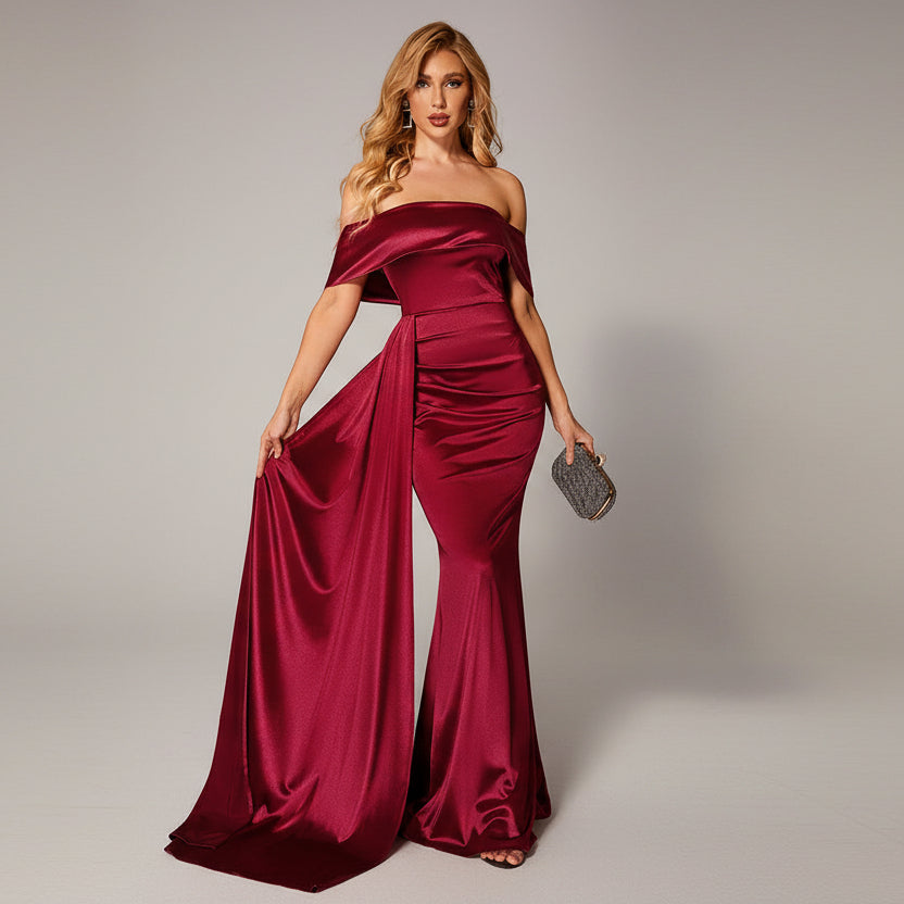 Woman in a burgundy evening gown holding a clutch in a dimly lit room.