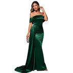 Woman in a green evening gown standing in front of a red couch against a dark background