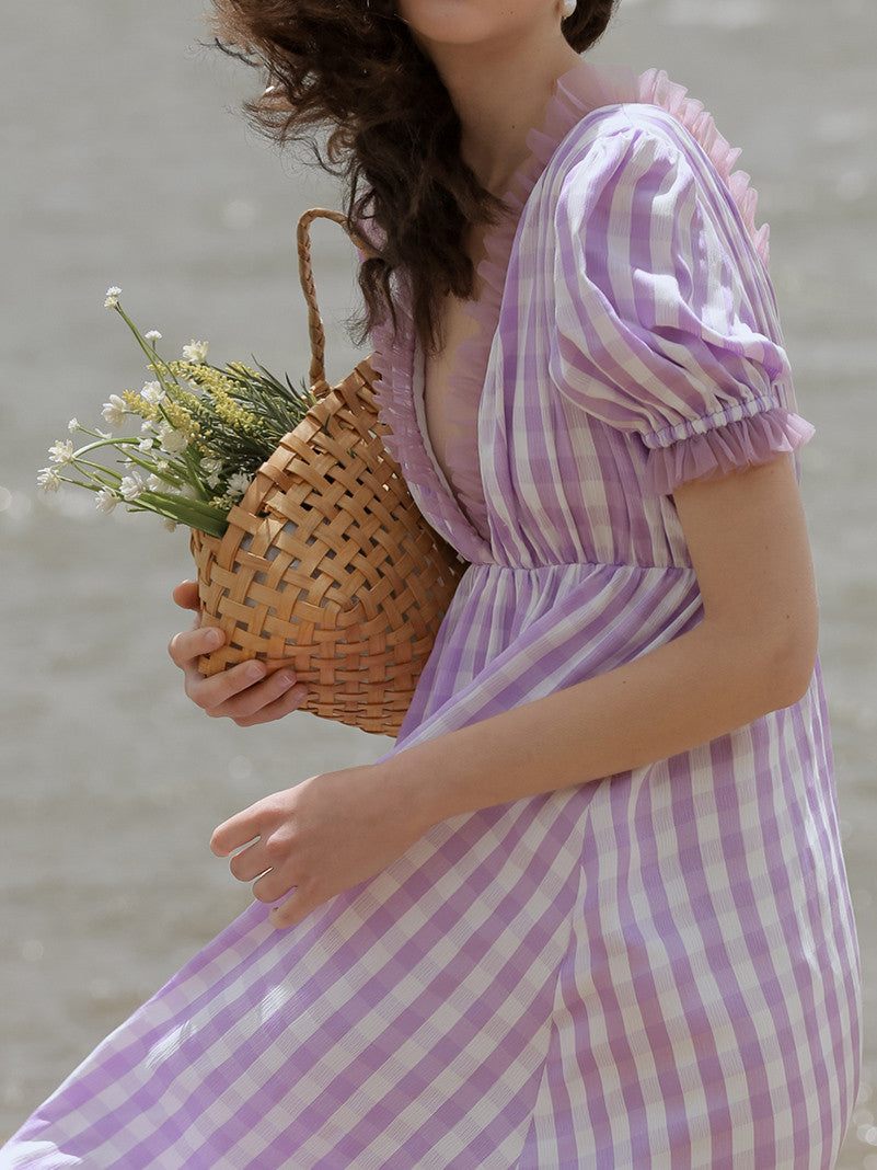 Woman in a purple and white striped dress holding a woven basket with plants against a blurred background