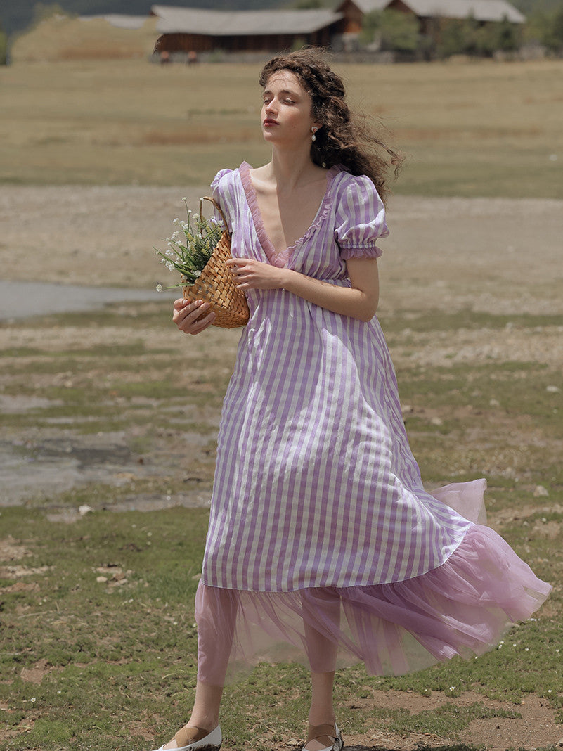 Woman in a purple checkered dress holding a woven basket with plants in a field.